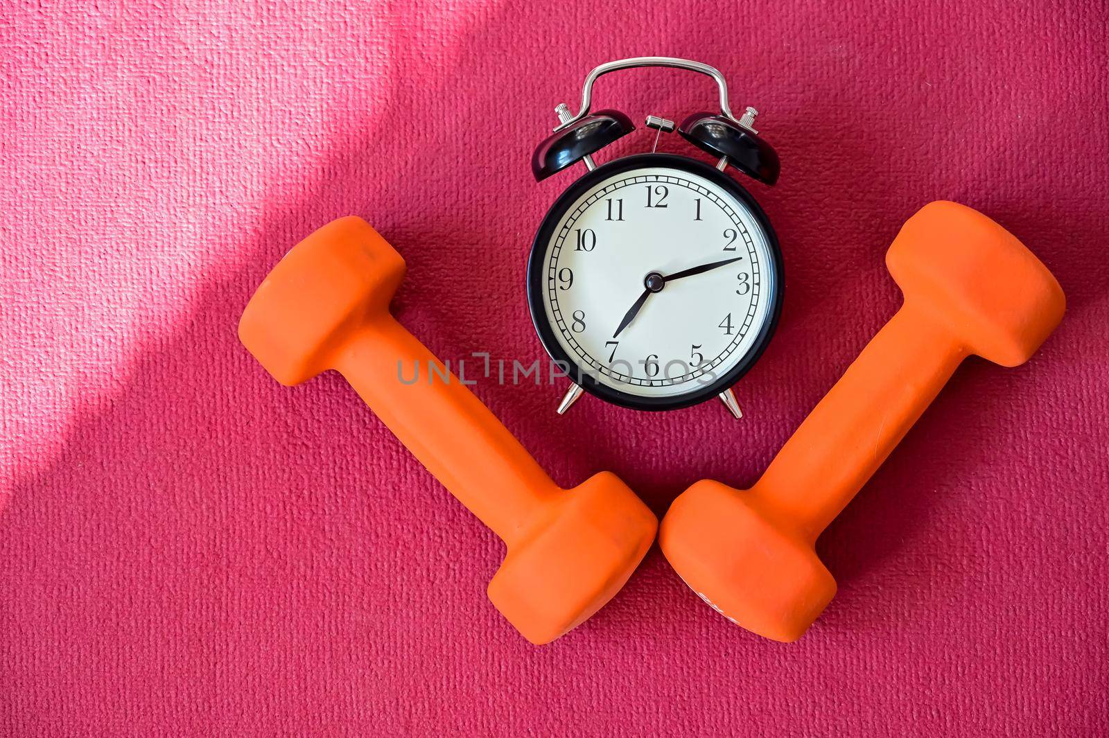 Two orange tunnels and an alarm clock on a pink yoga mat. Time to do fitness on self-isolation. Sports with equipment at home