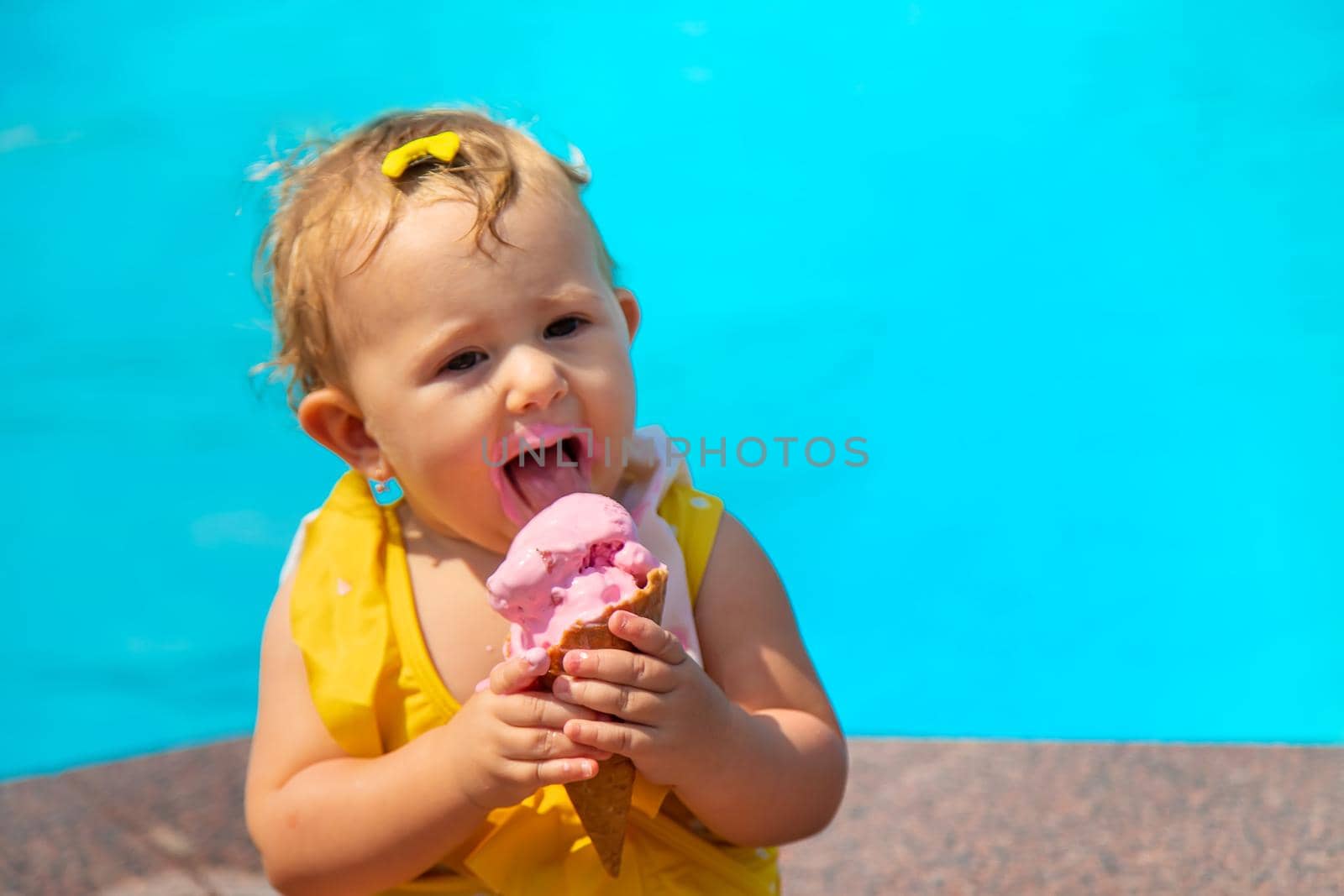 The child is eating ice cream near the pool. Selective focus. Kid.