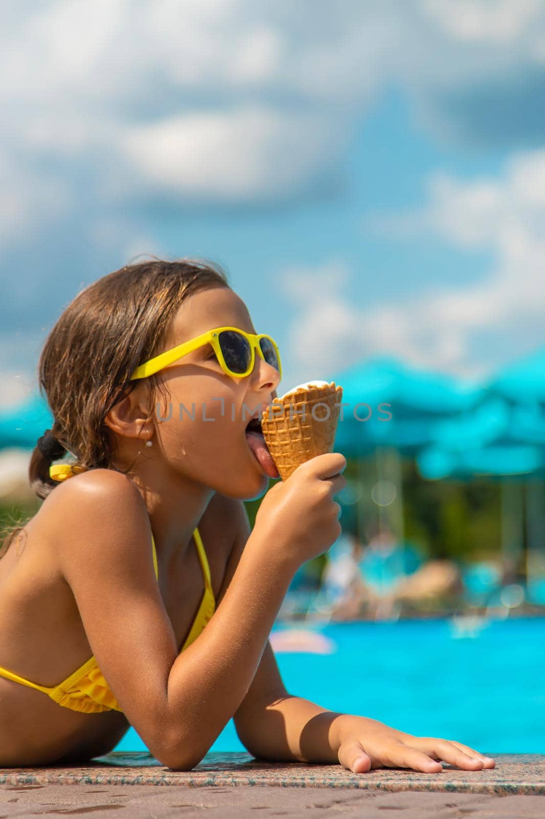 The child is eating ice cream near the pool. Selective focus. by yanadjana