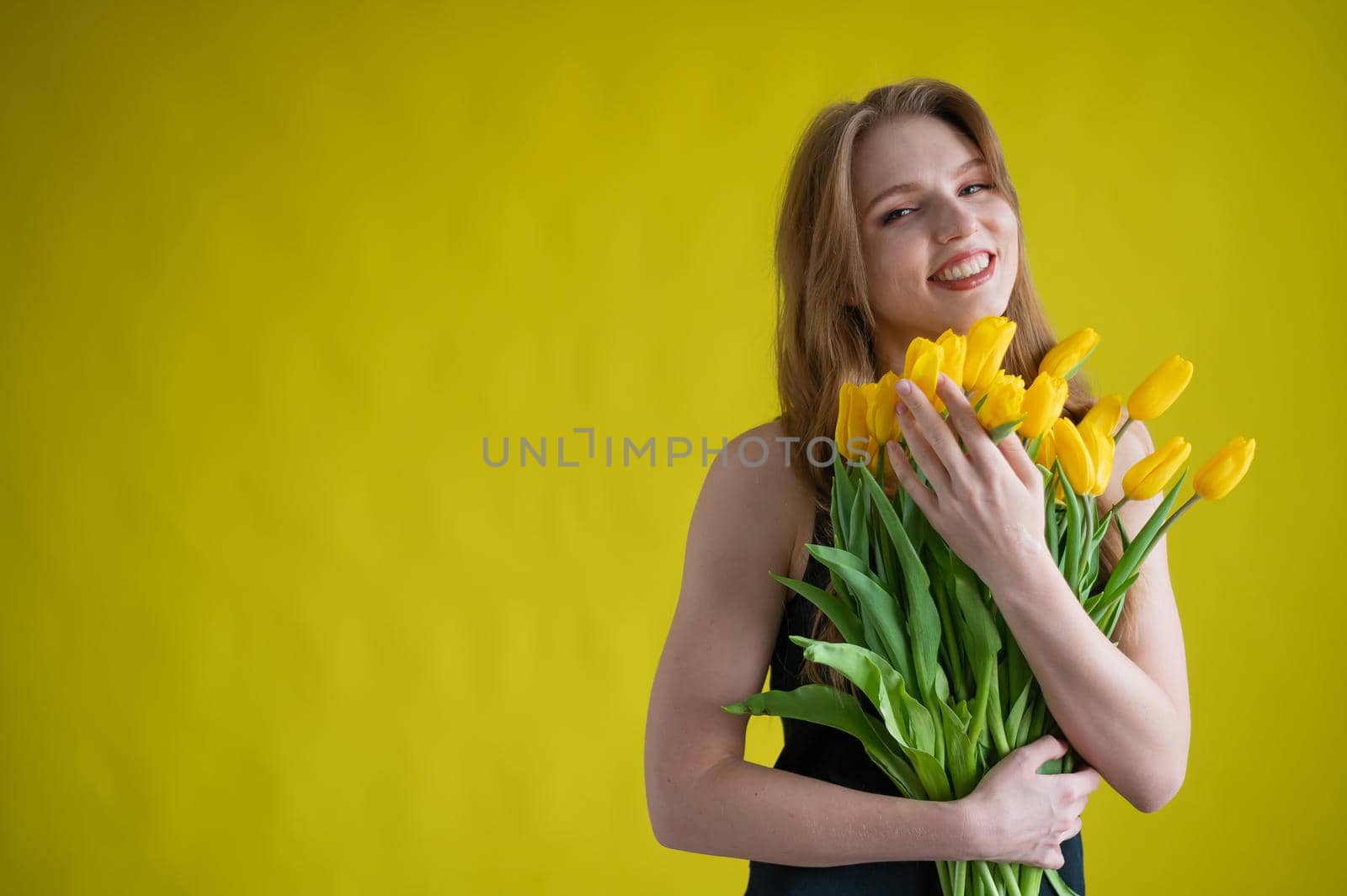 Caucasian woman with an armful of yellow tulips on a yellow background. International Women's Day. Bouquet of spring flowers by mrwed54