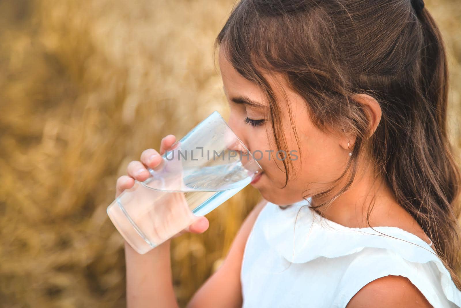 The child drinks water from a glass. Selective focus. Kid.