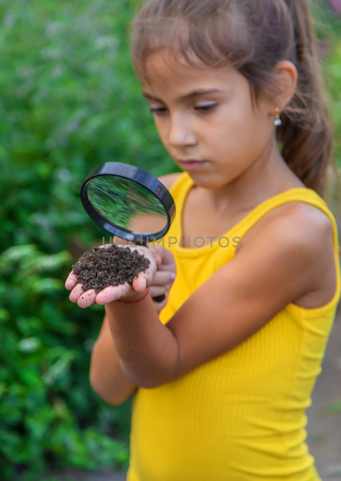 The child examines the ground with a magnifying glass. Selective focus. by yanadjana