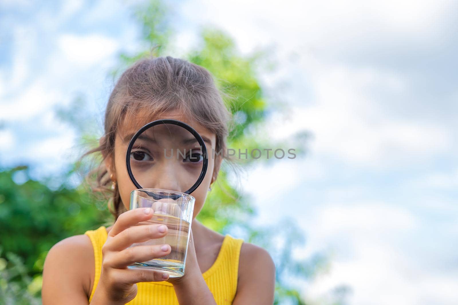 The child examines a glass of water with a magnifying glass. Selective focus. Kid.