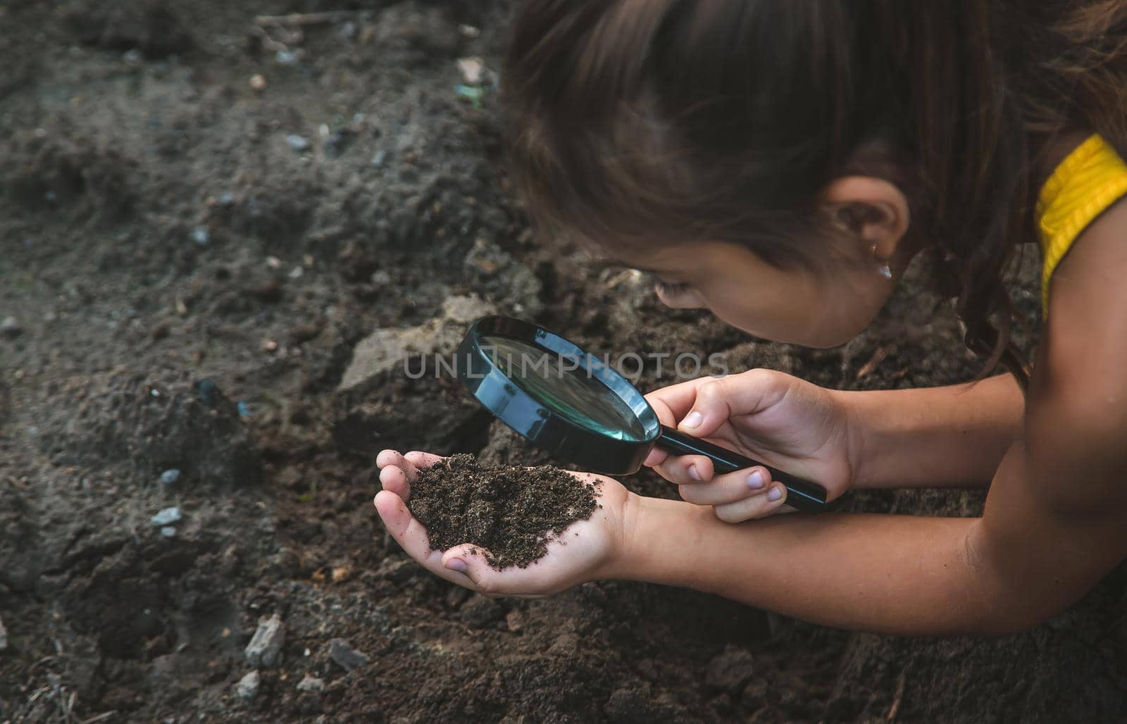 The child examines the ground with a magnifying glass. Selective focus. Nature.