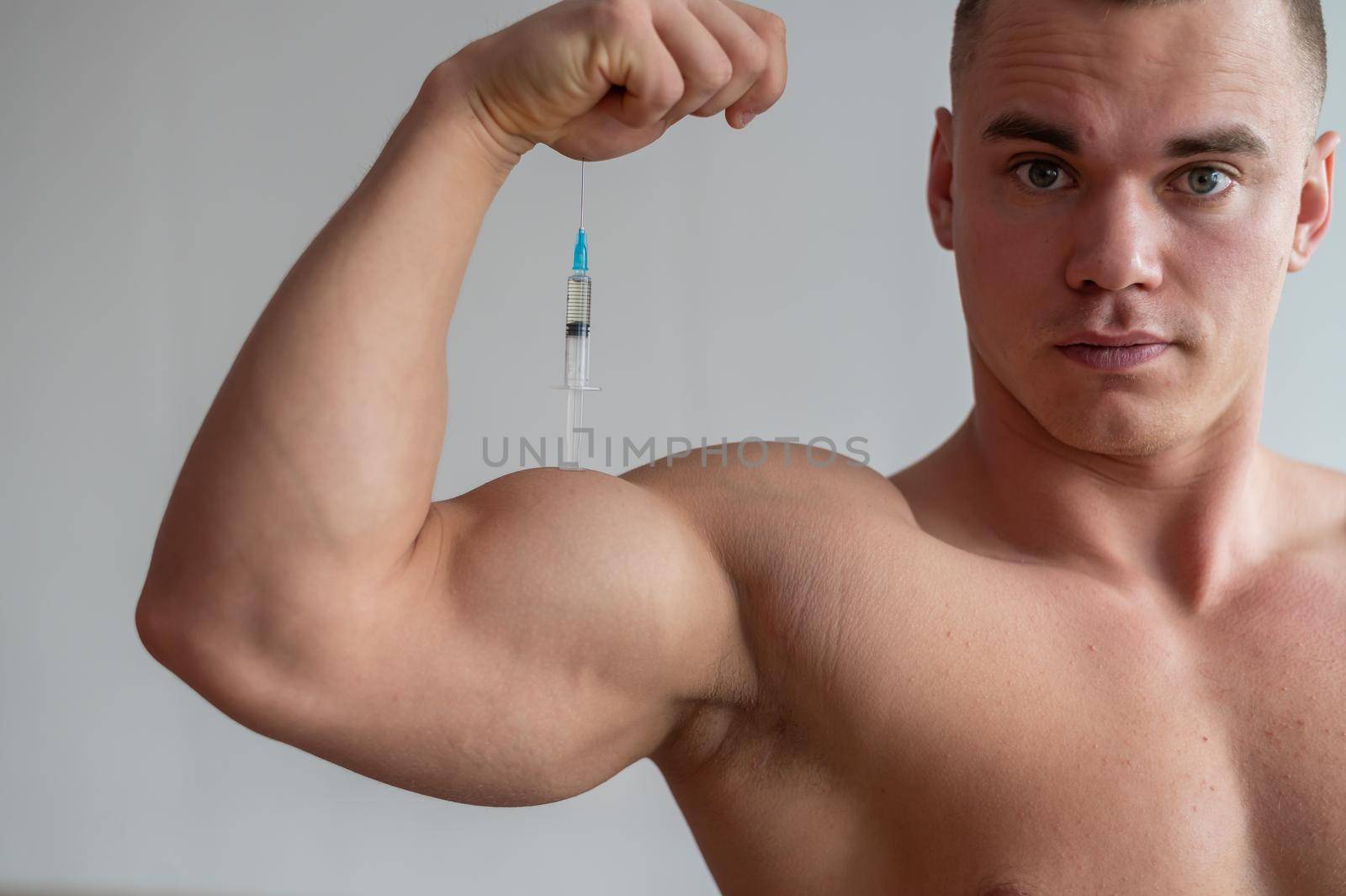 A muscular man with a naked torso holds a dope syringe. Attractive bodybuilder puts himself on steroids. Athlete cheats for gaining muscle mass