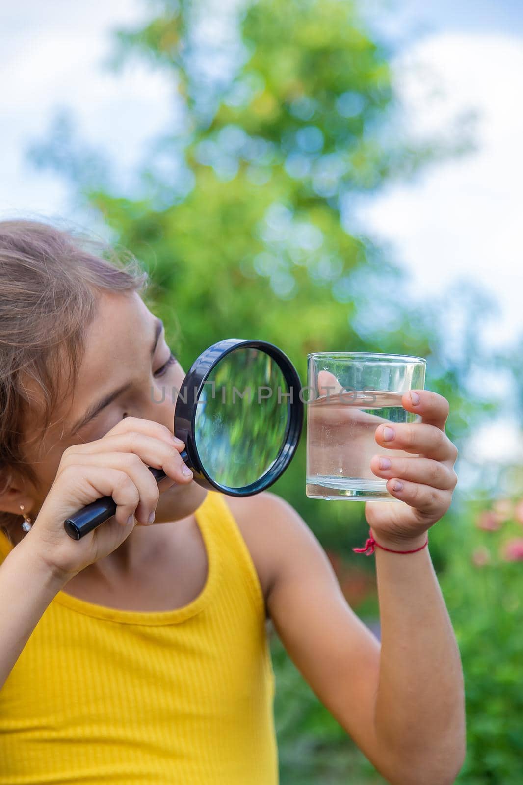 The child examines a glass of water with a magnifying glass. Selective focus. by yanadjana