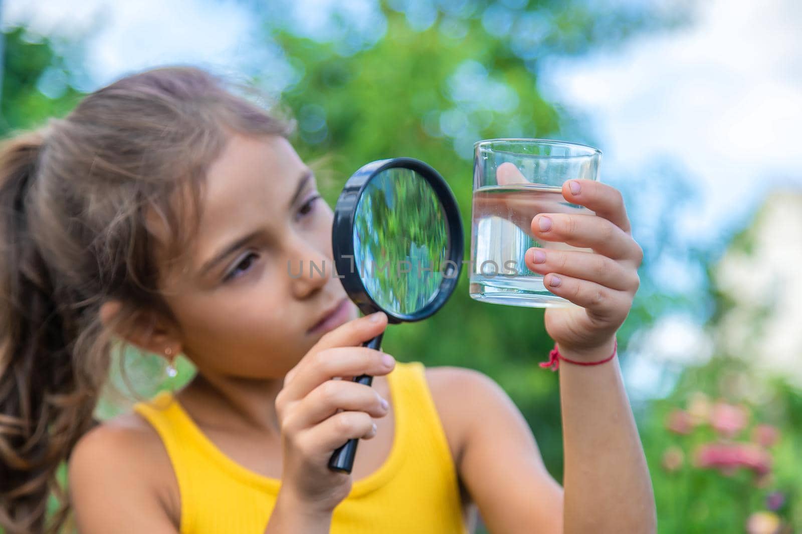 The child examines a glass of water with a magnifying glass. Selective focus. Kid.