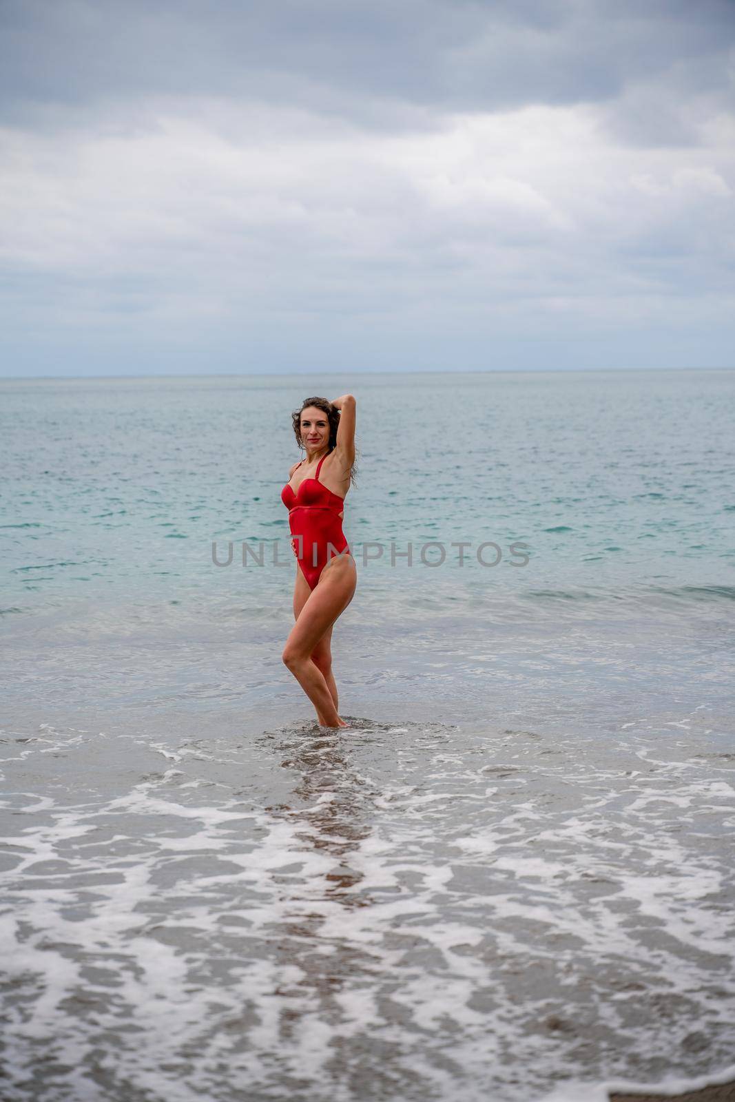 A beautiful and sexy brunette in a red swimsuit on a pebble beach, Running along the shore in the foam of the waves.