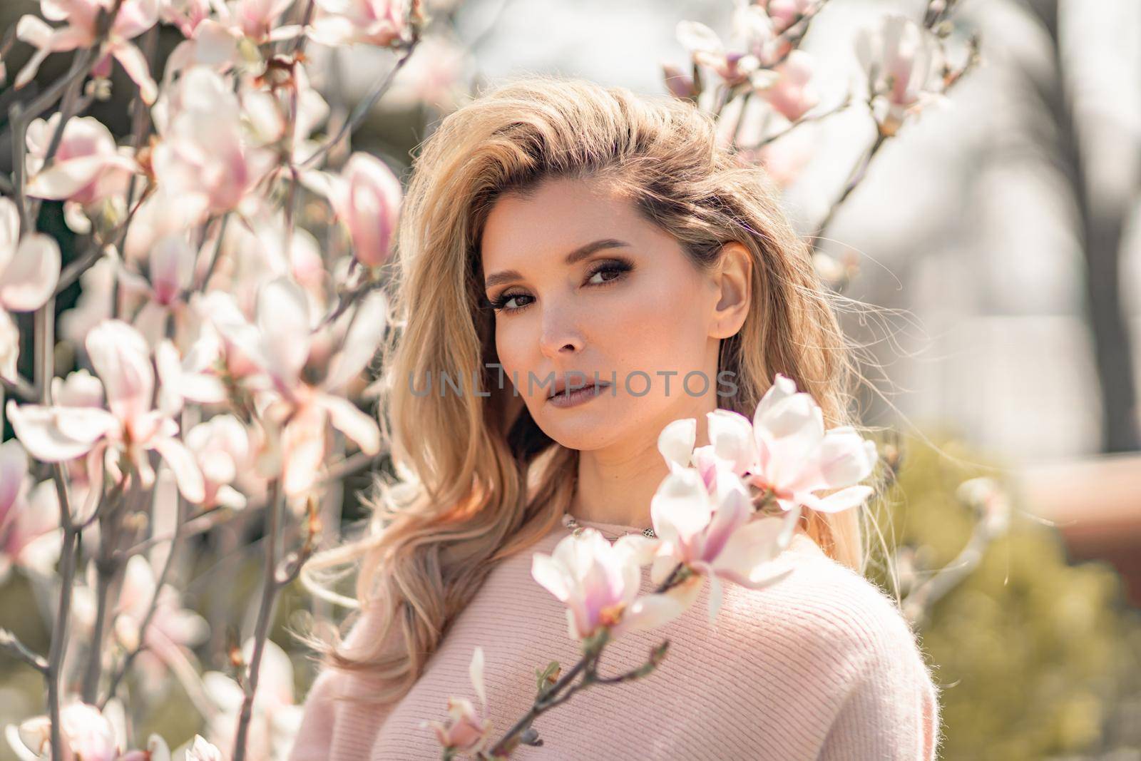 Portrait of a beautiful happy middle aged woman enjoying the smell in a blooming spring garden. Beautiful magnolia bushes, large flowers