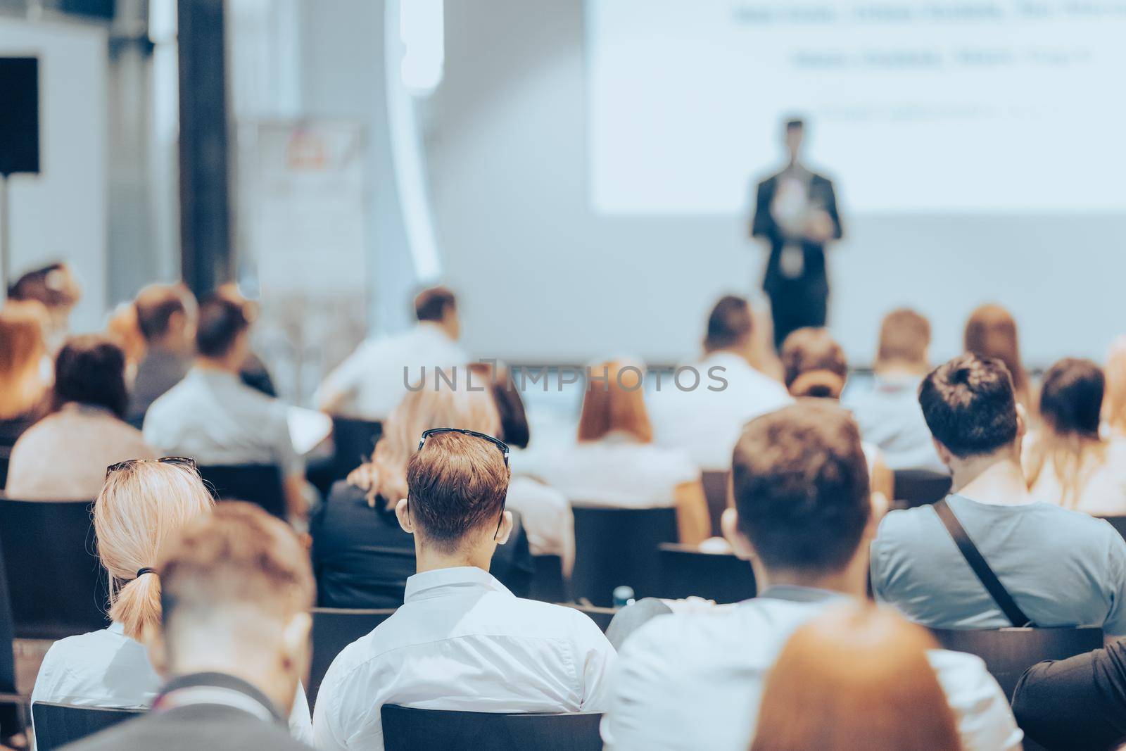 Speaker giving a talk in conference hall at business event. Rear view of unrecognizable people in audience at the conference hall. Business and entrepreneurship concept.