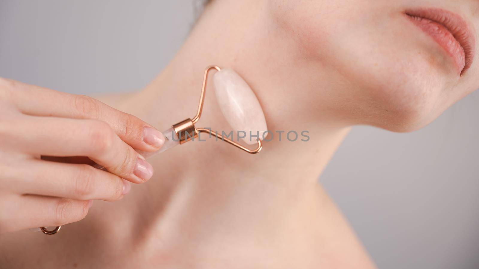 Close-up portrait of a woman using a quartz roller massager for an alternative fight against wrinkles on her neck. Smoothing of the rings of venus. by mrwed54