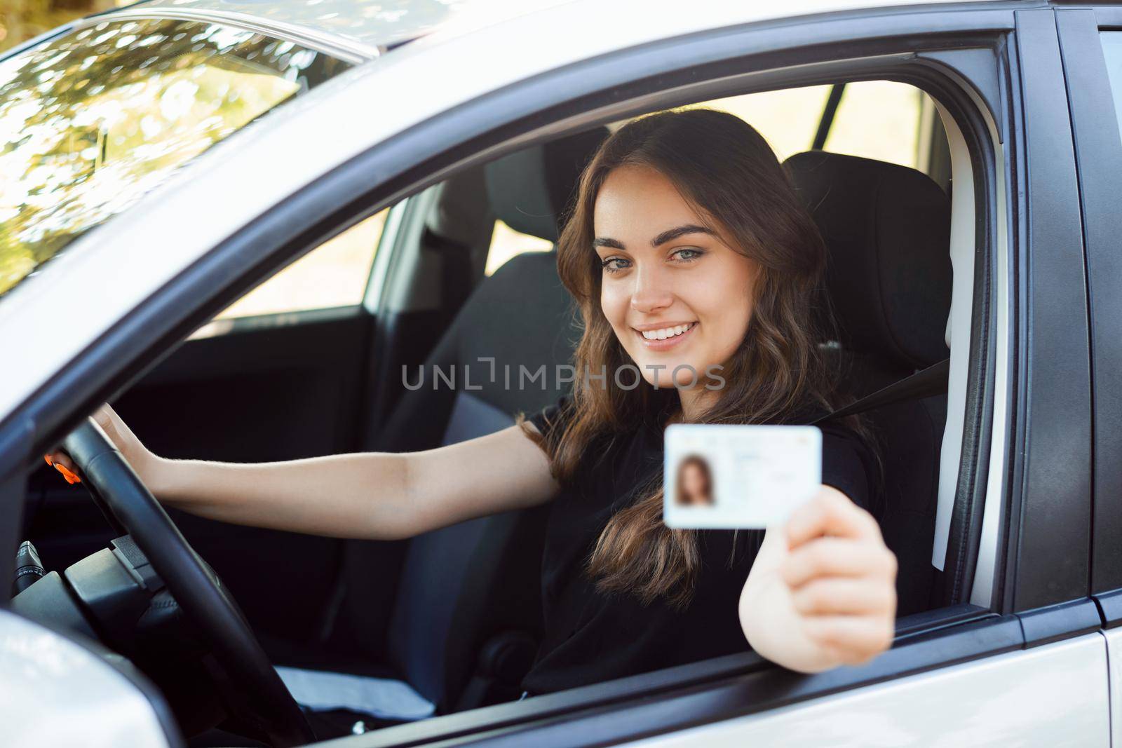 Female driver sitting in car and showing driving car license by VitaliiPetrushenko