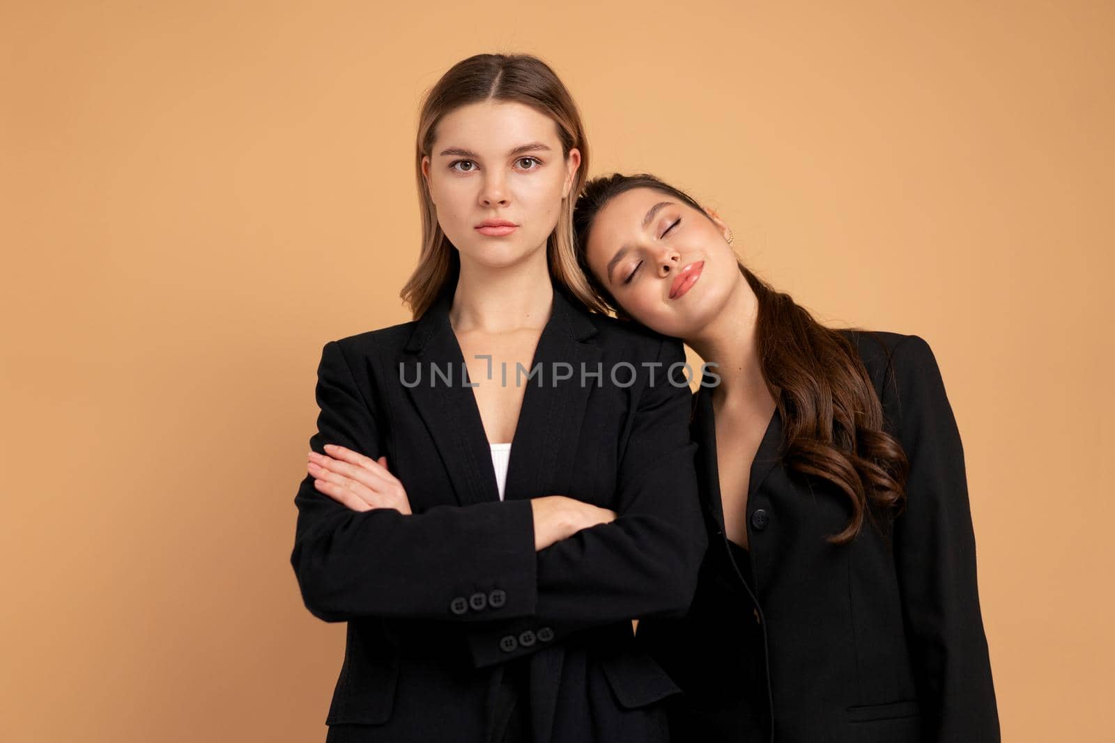 Two young business woman dressed black suit standing studio orange color background by andreonegin