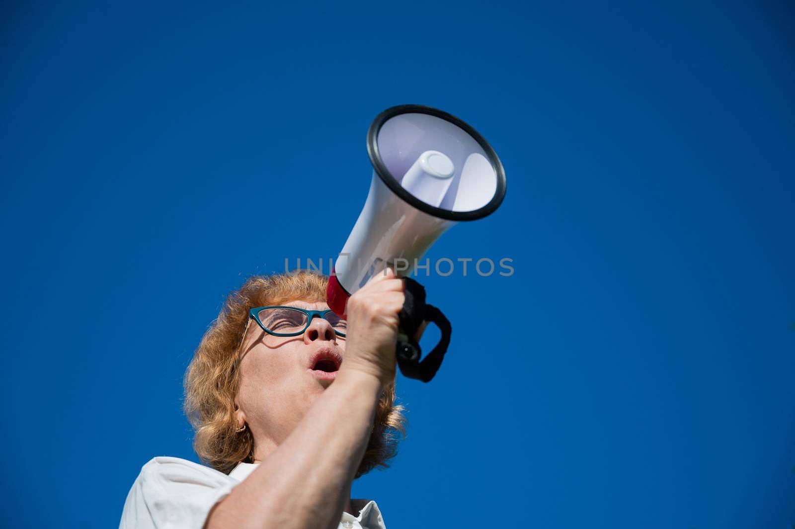 An emotional elderly woman pushes demands into a megaphone. An angry retired woman is fighting for the rights of older people. The female leader of the rally voiced claims to the loudspeaker