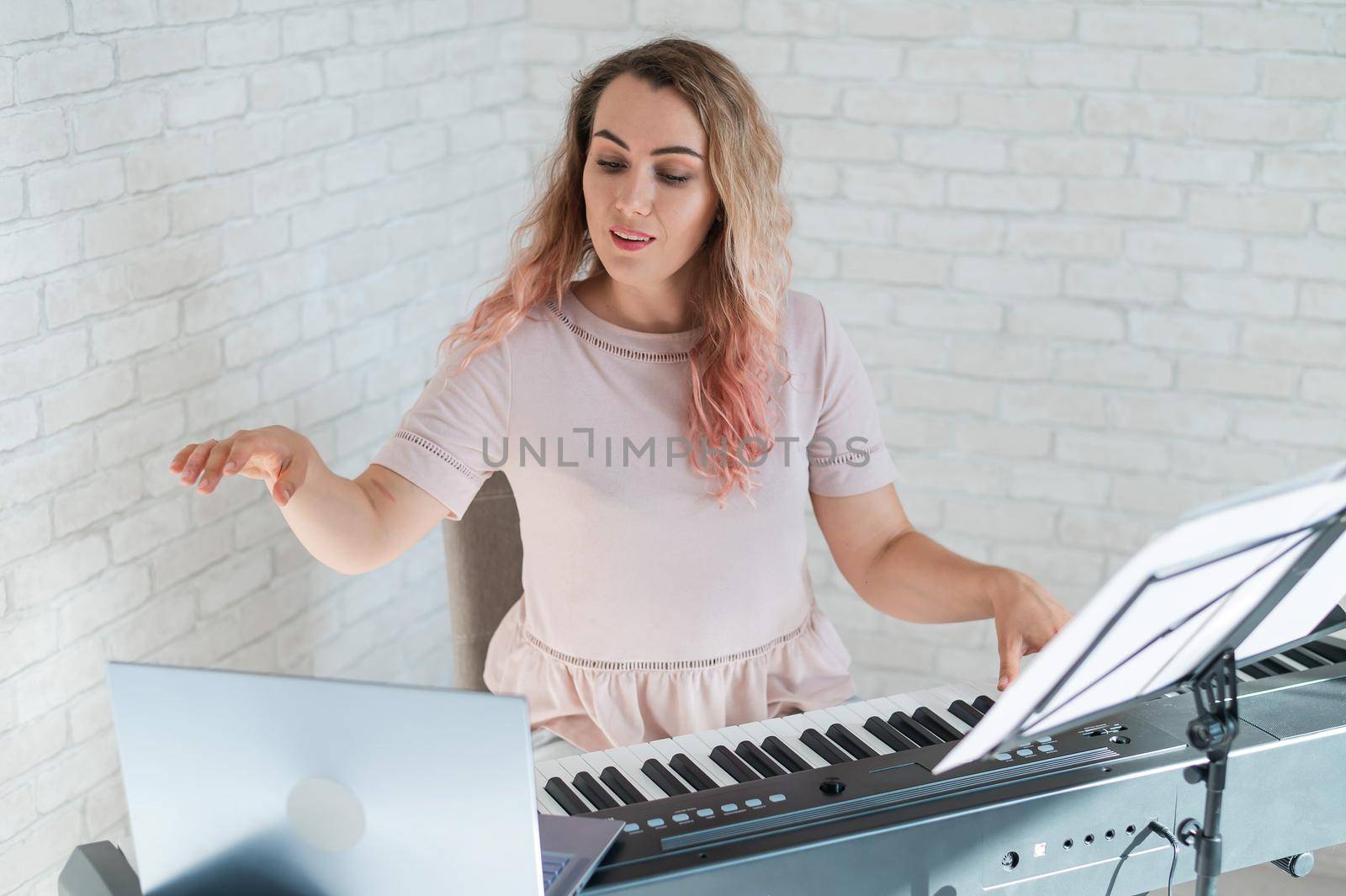 A friendly woman plays the electronic piano and conducts a video blog on her laptop. Stay home. Musical instrument teacher. Distance learning music quarantined