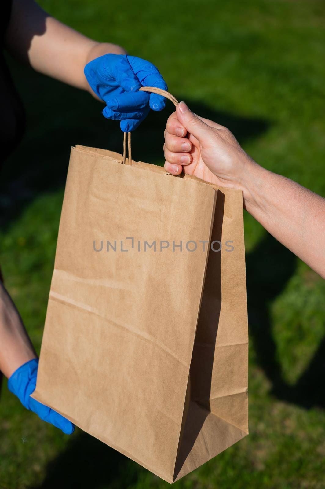 Faceless courier in gloves hands an eco friendly old lady's paper bag in the park. The concept of order delivery anywhere. Caring for the environment. Recyclable packaging. Close-up