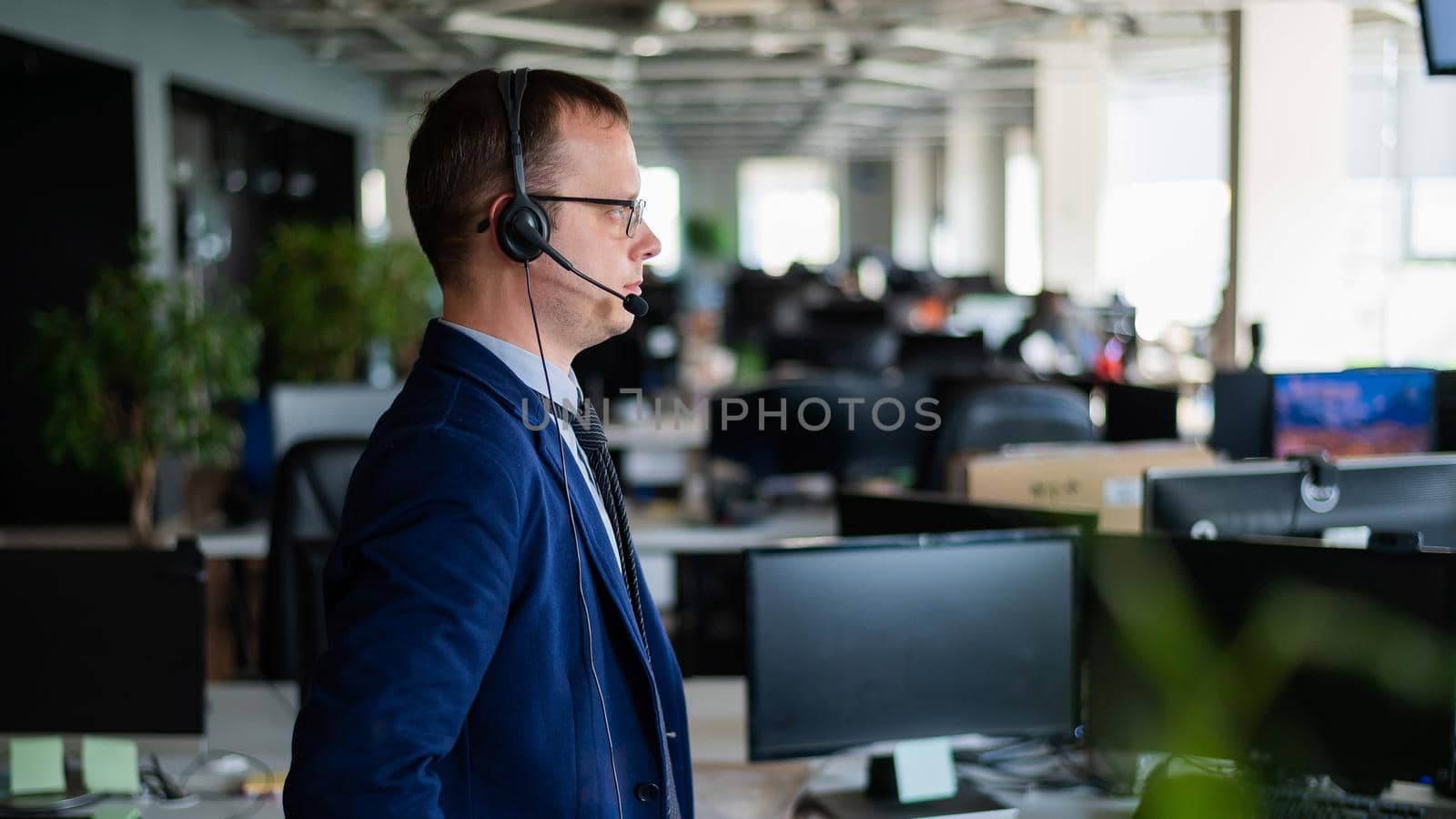 Portrait of a male call center operator in headset at workplace. A man works in an open space office answering customer calls. Support service or hotline. Agent of a telemarketing company