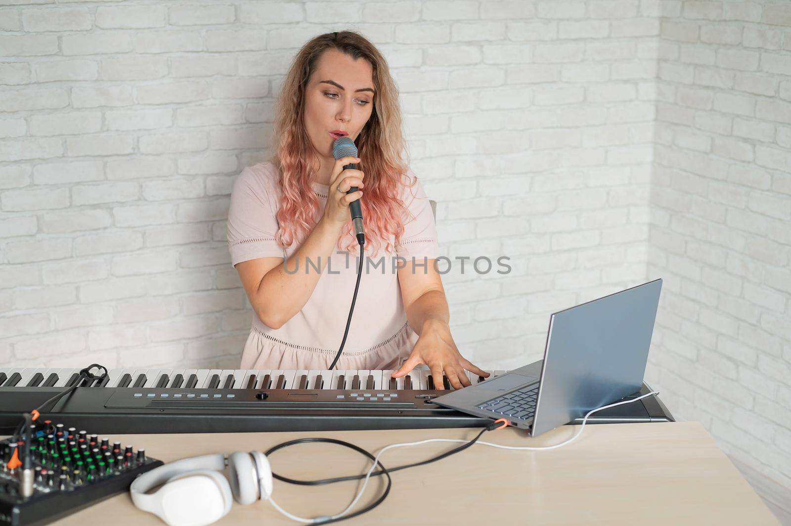 A woman records a vocal lesson using a laptop and accompanying on a keyboard while at home. The teacher sings a song into the microphone and plays the electronic piano. A blogger is recording a video