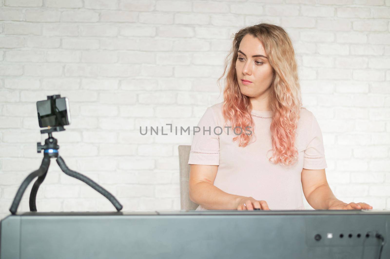 A woman plays the electronic piano and conducts a video blog on a smartphone. A girl takes video from a phone on a tripod. Female music teacher works remotely. by mrwed54