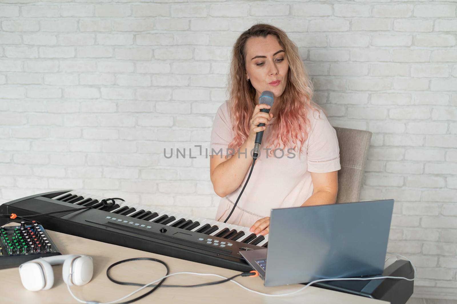 A woman records a vocal lesson using a laptop and accompanying on a keyboard while at home. The teacher sings a song into the microphone and plays the electronic piano. A blogger is recording a video