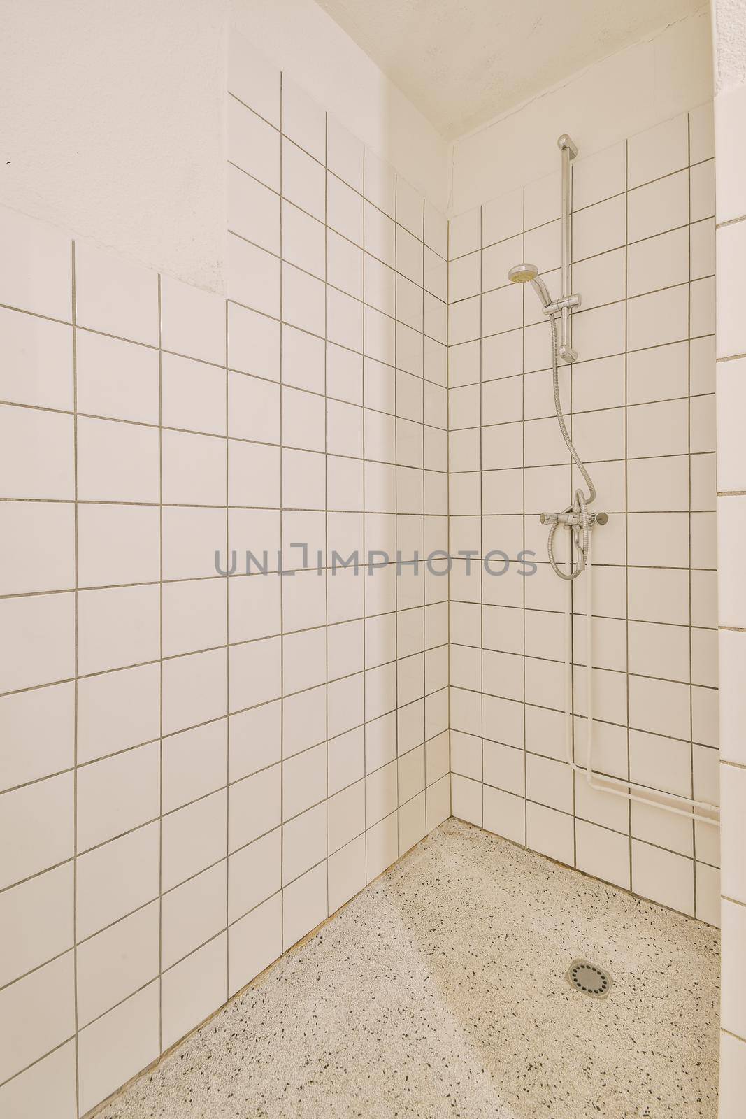 Shower faucets attached to tiled wall near glass partition and ornamental curtail in washroom at home