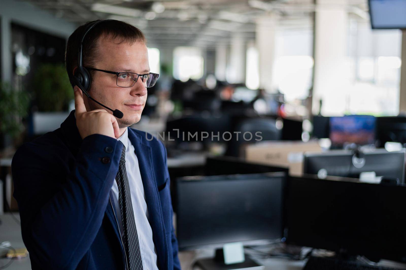 A friendly man from a call center answers a customer with a hands-free headset. Male helpdesk operator talking on the phone. Manager in open space office