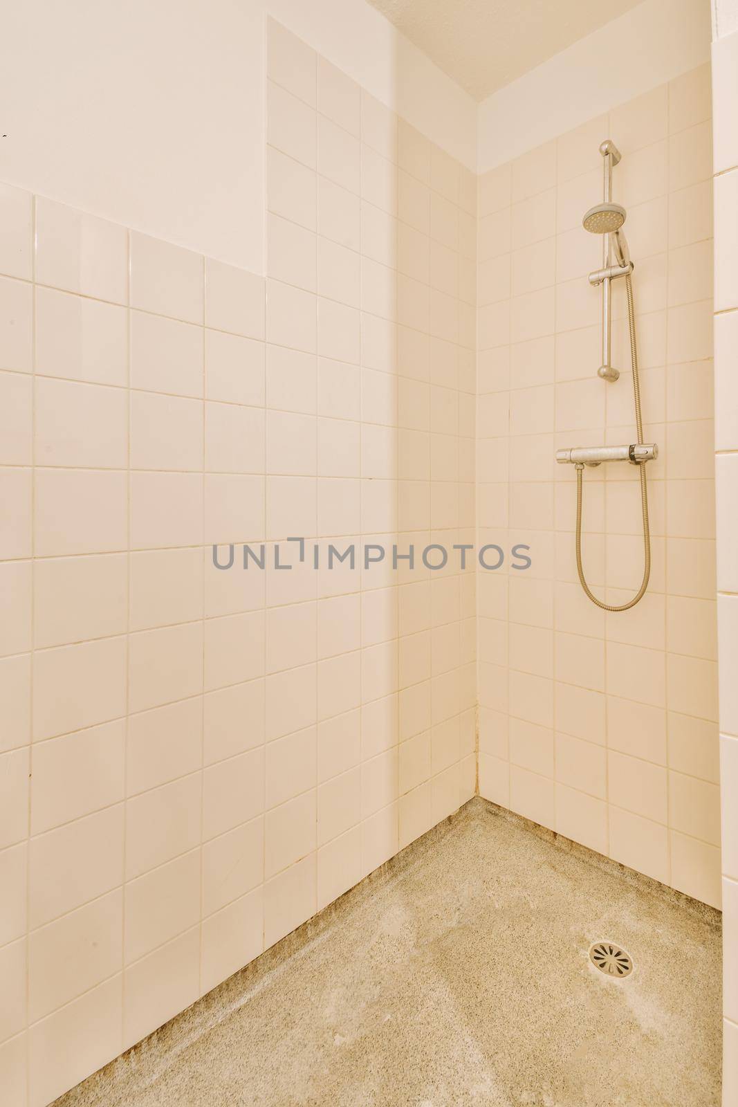 Shower faucets attached to tiled wall near glass partition and ornamental curtail in washroom at home