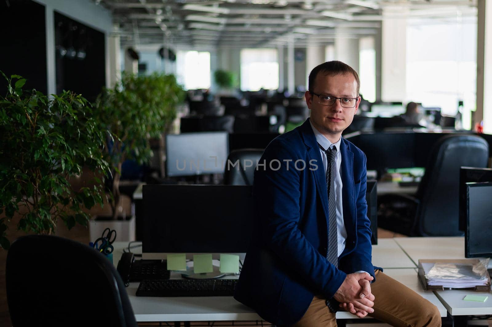 Happy male employee at the workplace in the office Open Space. Friendly business man in a suit at his desk. Work in Modern office