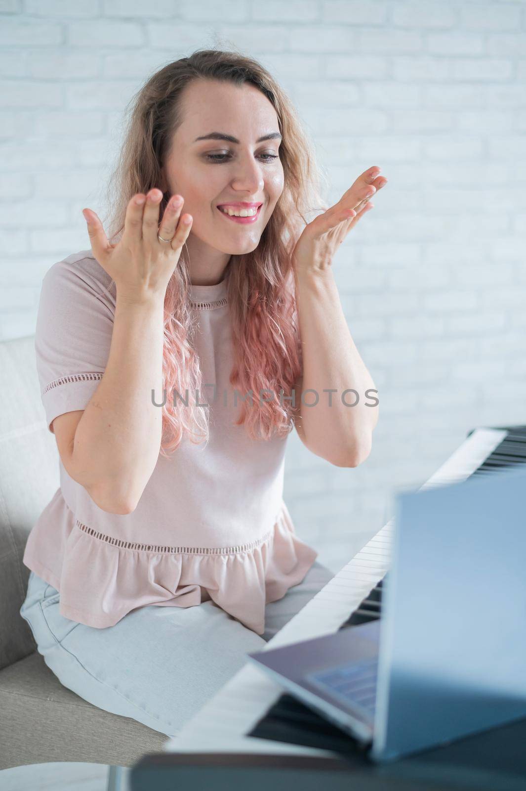 A friendly woman plays the electronic piano and conducts a video blog on her laptop. Stay home. Musical instrument teacher. Distance learning music quarantined