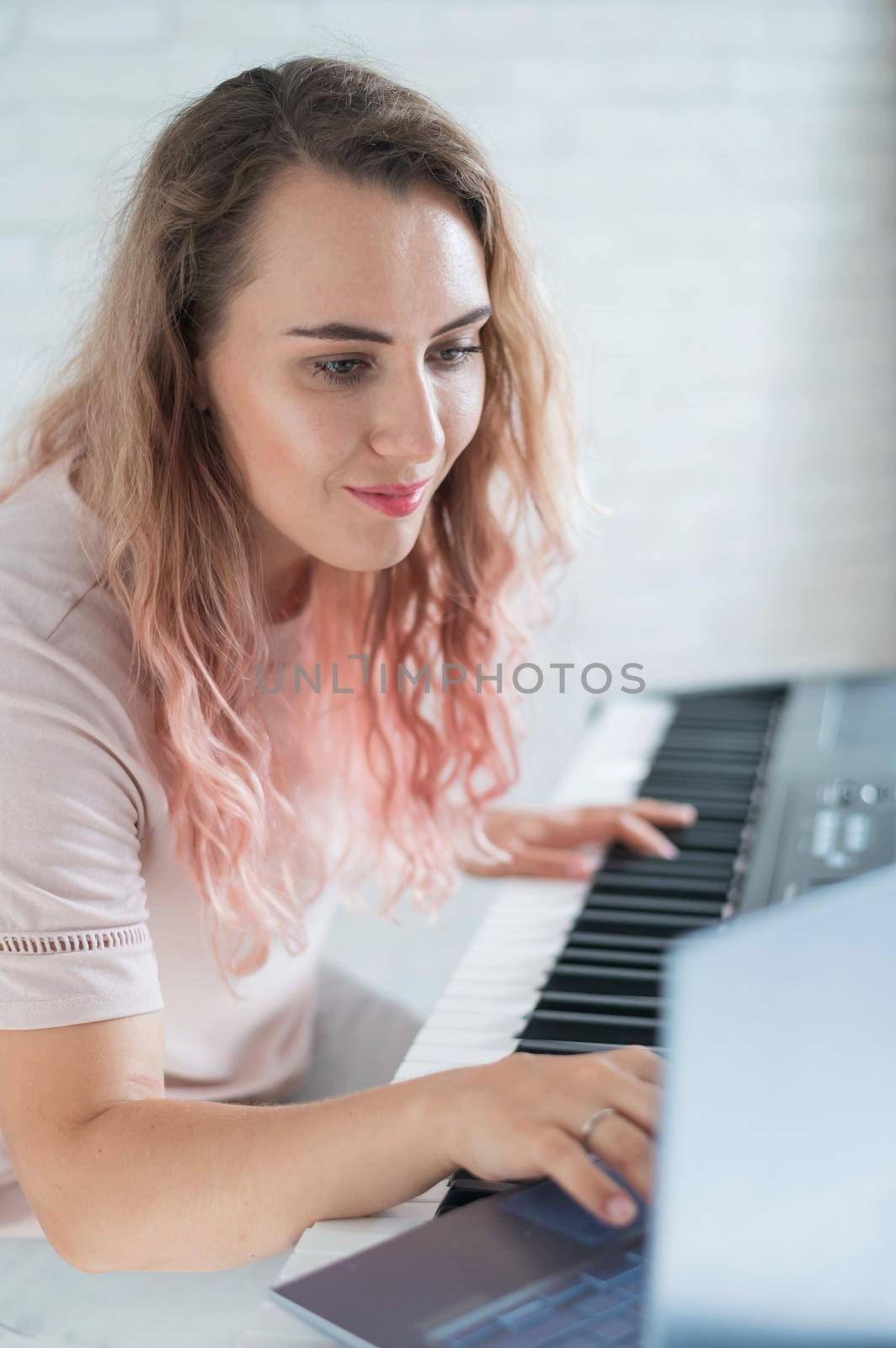 A friendly woman plays the electronic piano and conducts a video blog on her laptop. Stay home. Musical instrument teacher. Distance learning music quarantined. by mrwed54