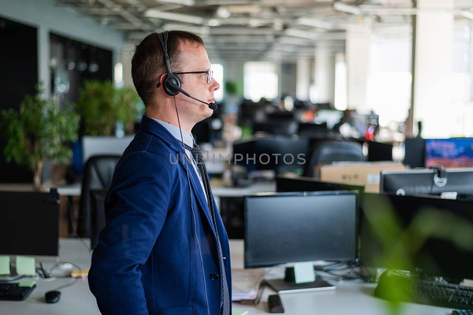 Portrait of a male call center operator in headset at workplace. A man works in an open space office answering customer calls. Support service or hotline. Agent of a telemarketing company