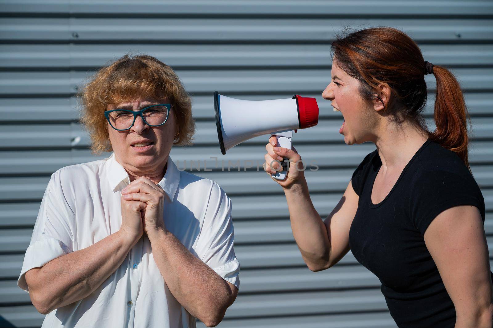 The conflict of generations. An angry middle-aged woman yells at an elderly mother through a megaphone. An adult daughter screams at an unhappy pensioner over a loudspeaker. Quarrel in the family. by mrwed54