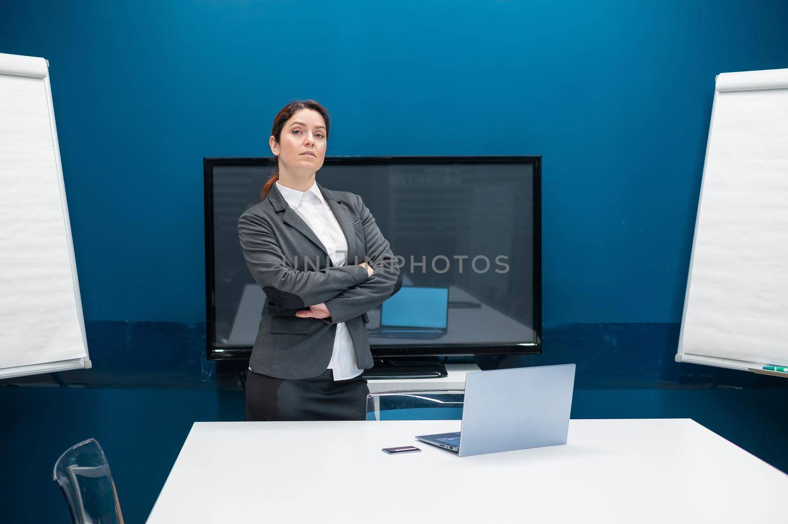 Serious woman dressed in a suit is having an online conversation on a laptop in a conference room. Female business coach conducts training. Remote negotiations in quarantine