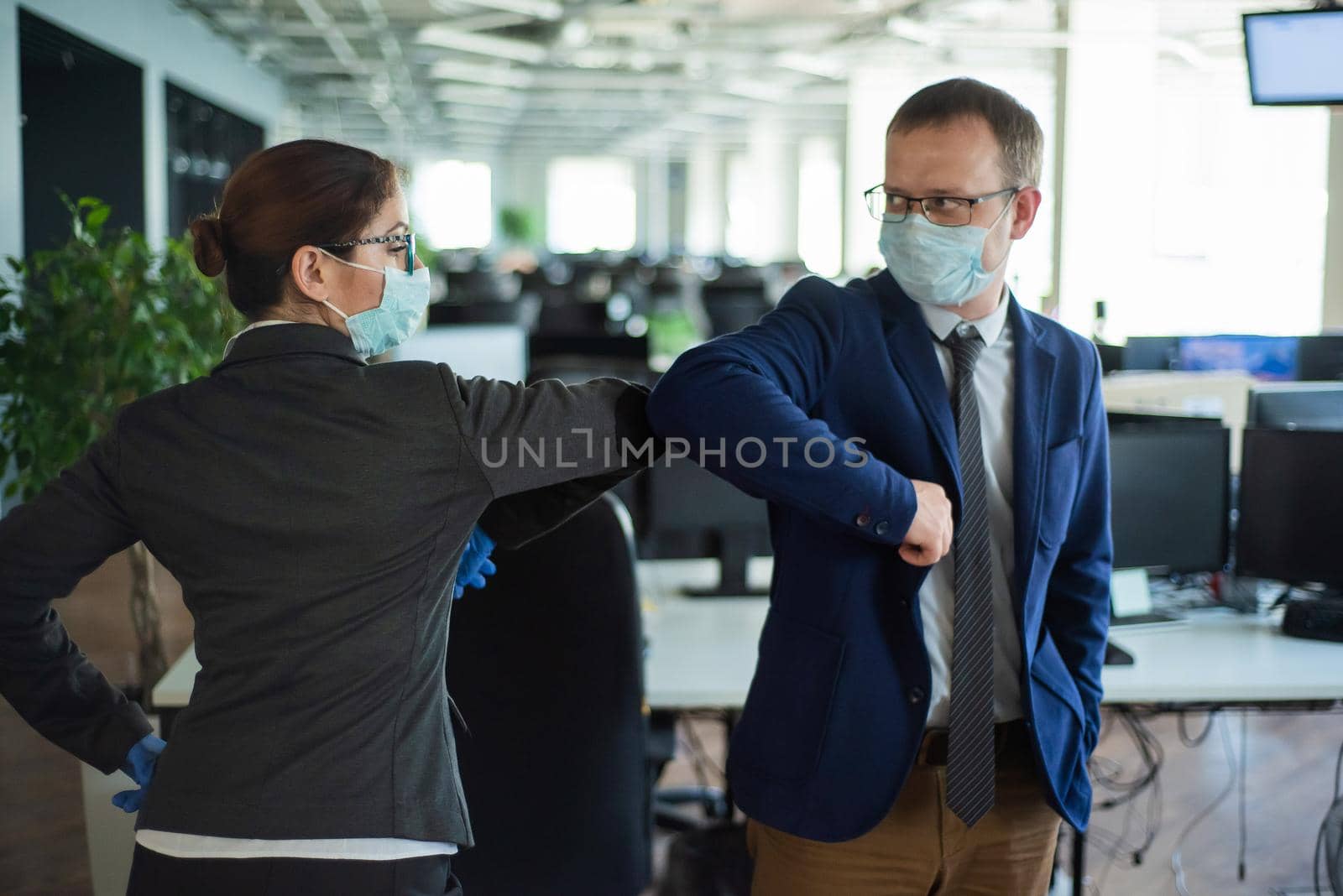 Office workers shake hands when meeting and greet bumping elbows. A new way to greet the obstructing spread of coronavirus. Man and woman in protective masks maintain a social distance at work