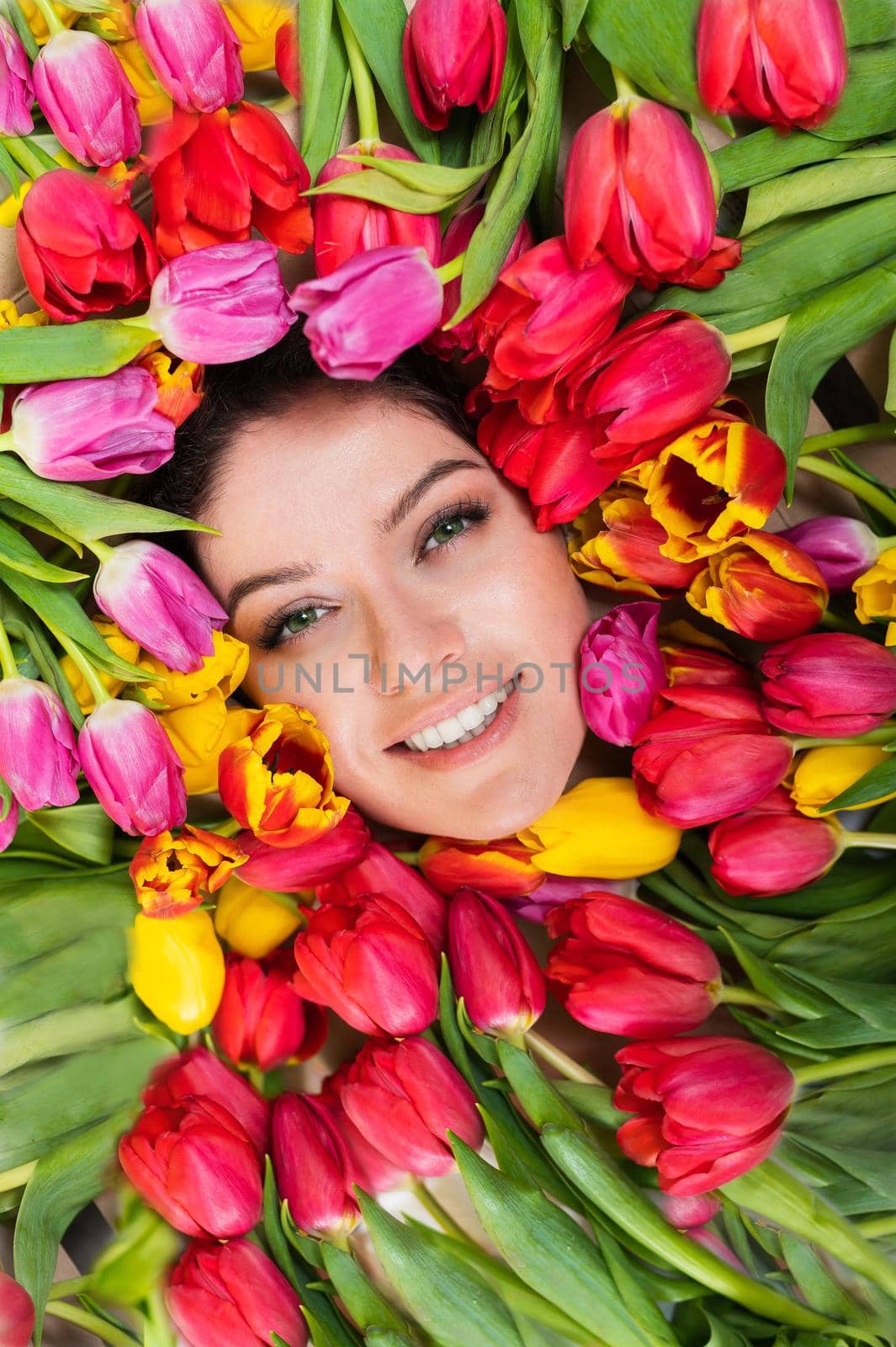 Portrait of a young beautiful woman with tulips around her face. The girl lies in the flowers given for March 8th. International Women's Day