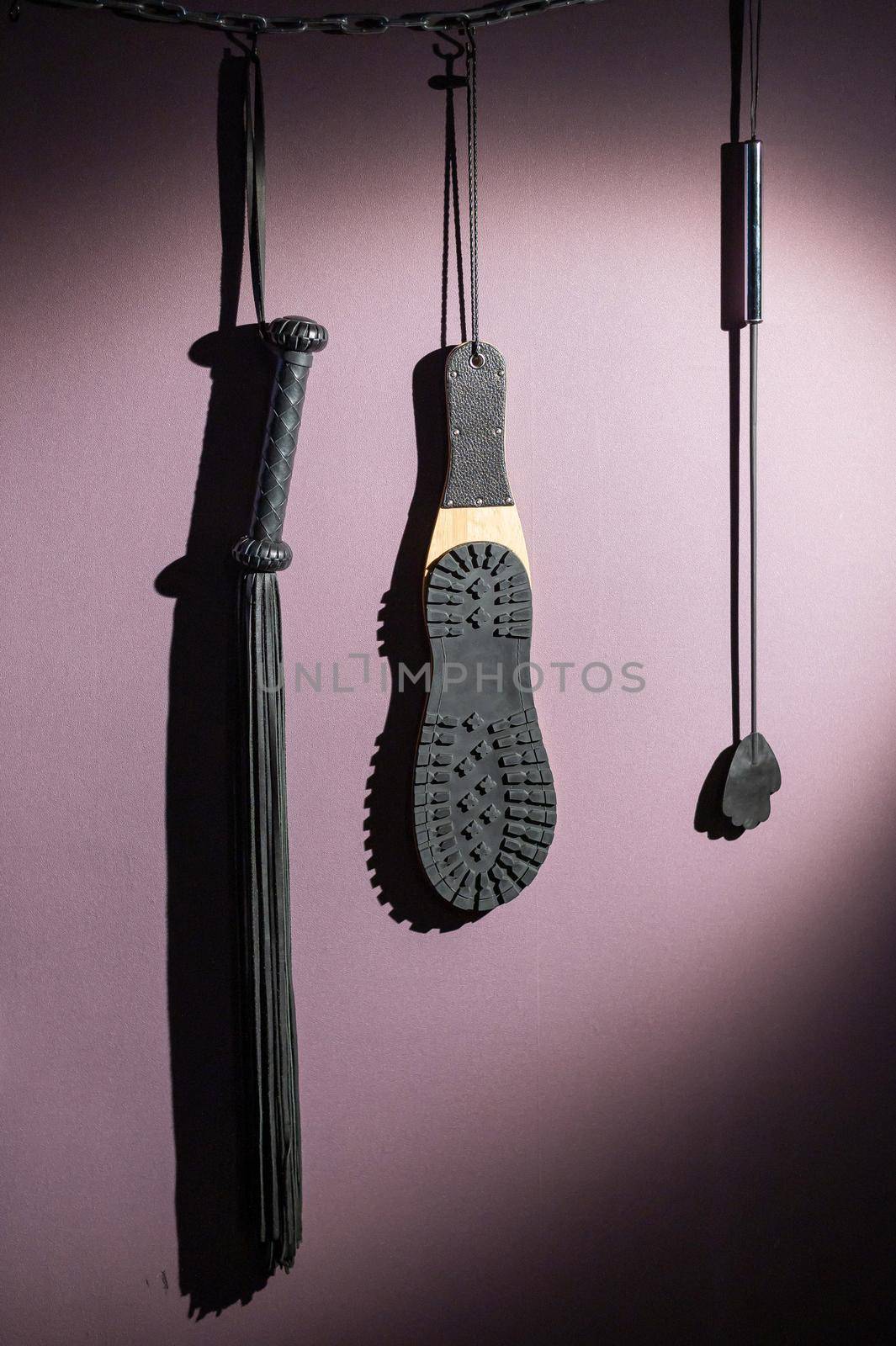 A diverse collection of leather lashes with fringe and a sole for sexual pleasures are hanging on the wall. Sex equipment for punishment and spanking for role-playing games. BDSM room. by mrwed54