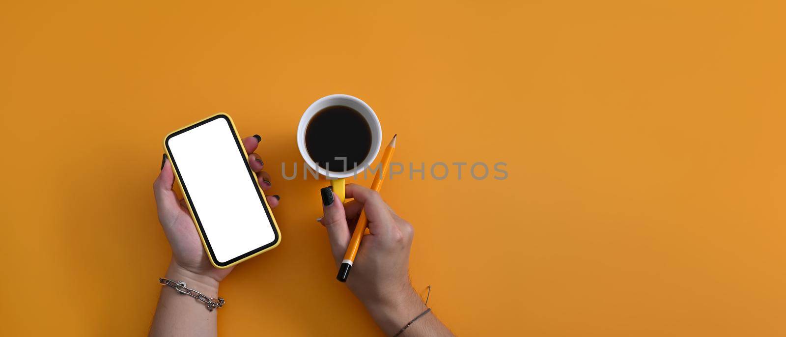 Woman holding mockup smart phone and coffee cup on yellow background with copy space. by prathanchorruangsak