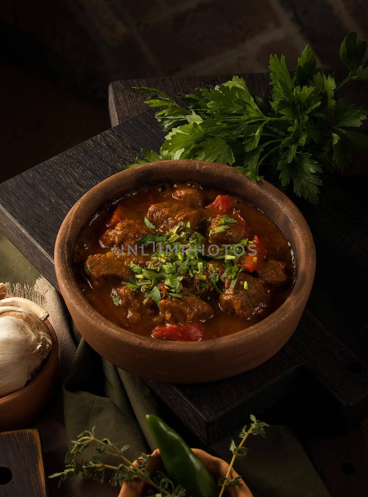 A close up shot of a meat stew and herbs in the background