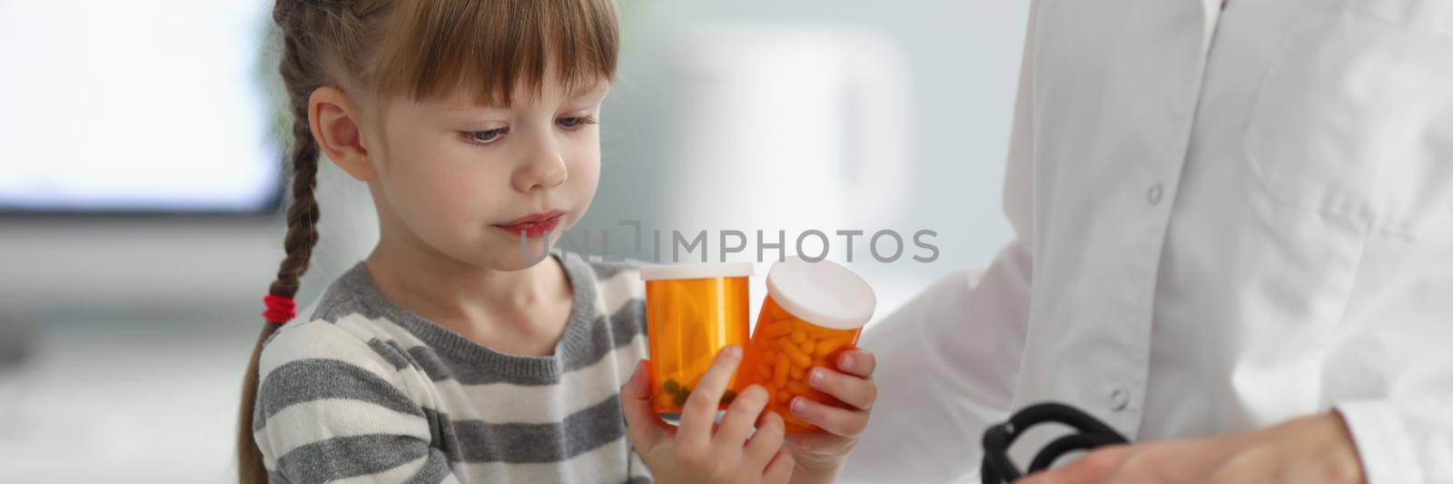 Portrait of child playing with bottles full of medication while on doctors appointment. Female doctor hold stethoscope for examining. Pediatrician concept