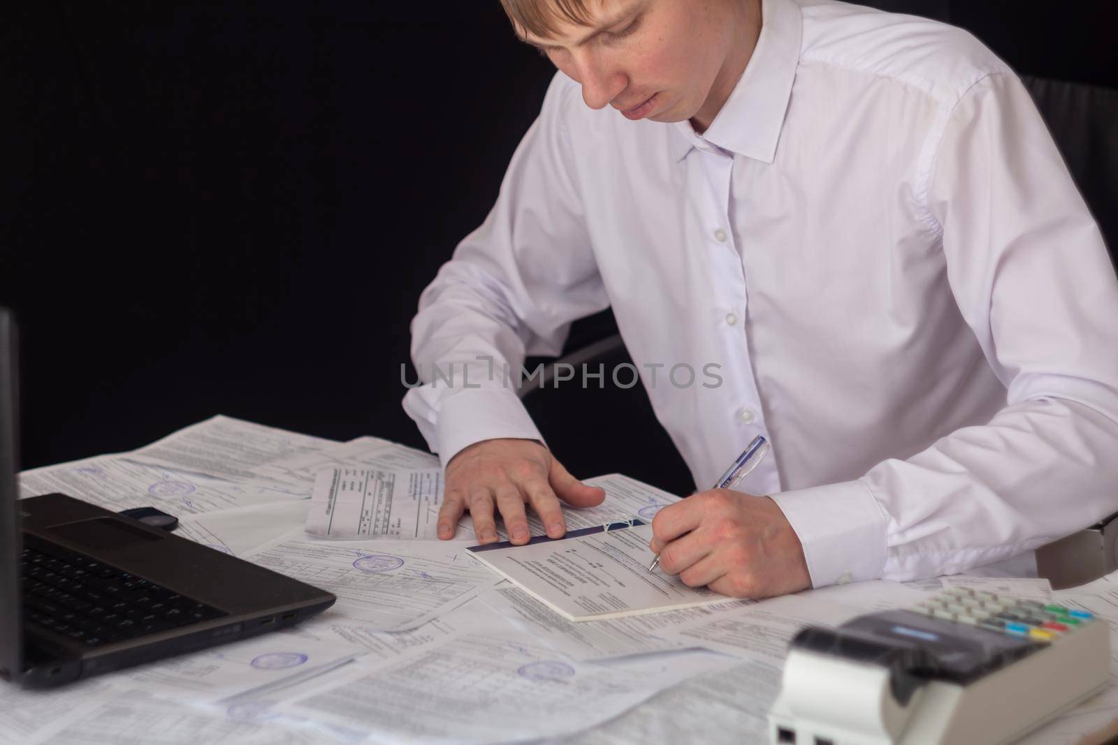 A businessman works with stocks, bonds, obligations, securities and documents in a night office. Fulfillment of obligations to work with documents in the office. Employee at a laptop in the office. by YevgeniySam