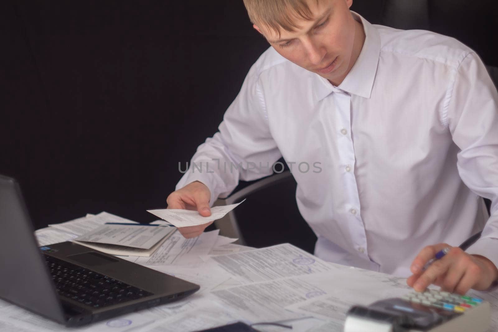 A businessman works with stocks, bonds, obligations, securities and documents in a night office. Fulfillment of obligations to work with documents in the office. Employee at a laptop in the office. by YevgeniySam