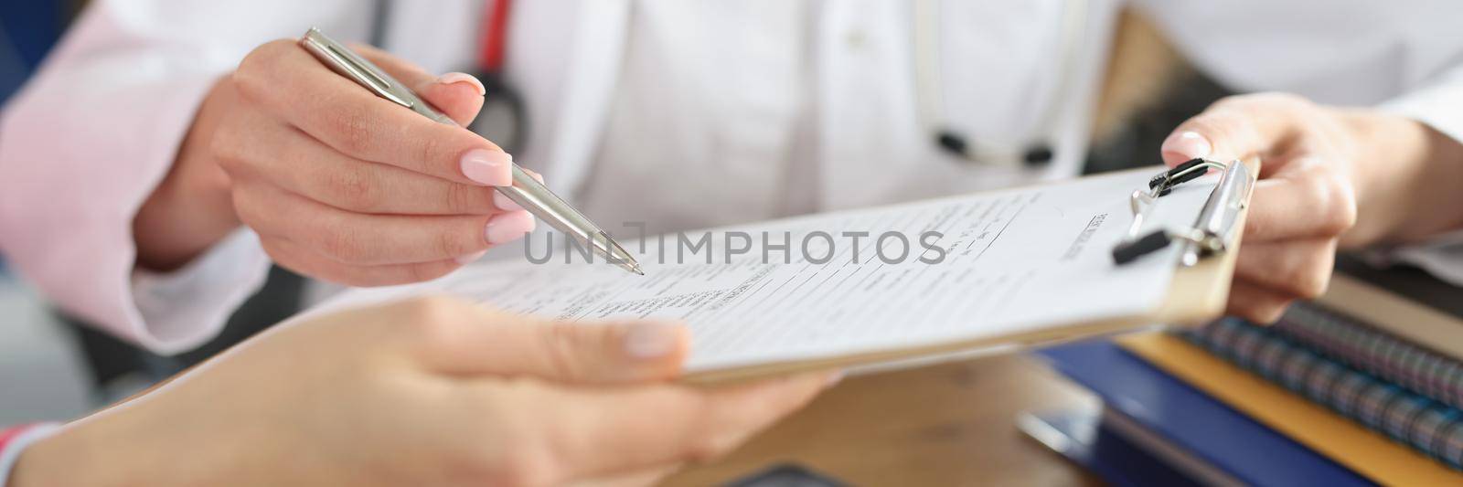 Close-up of doctor and patient signing medical contract. Physician pointing on place for signature. Prescription or medical insurance. Medicine and healthcare concept