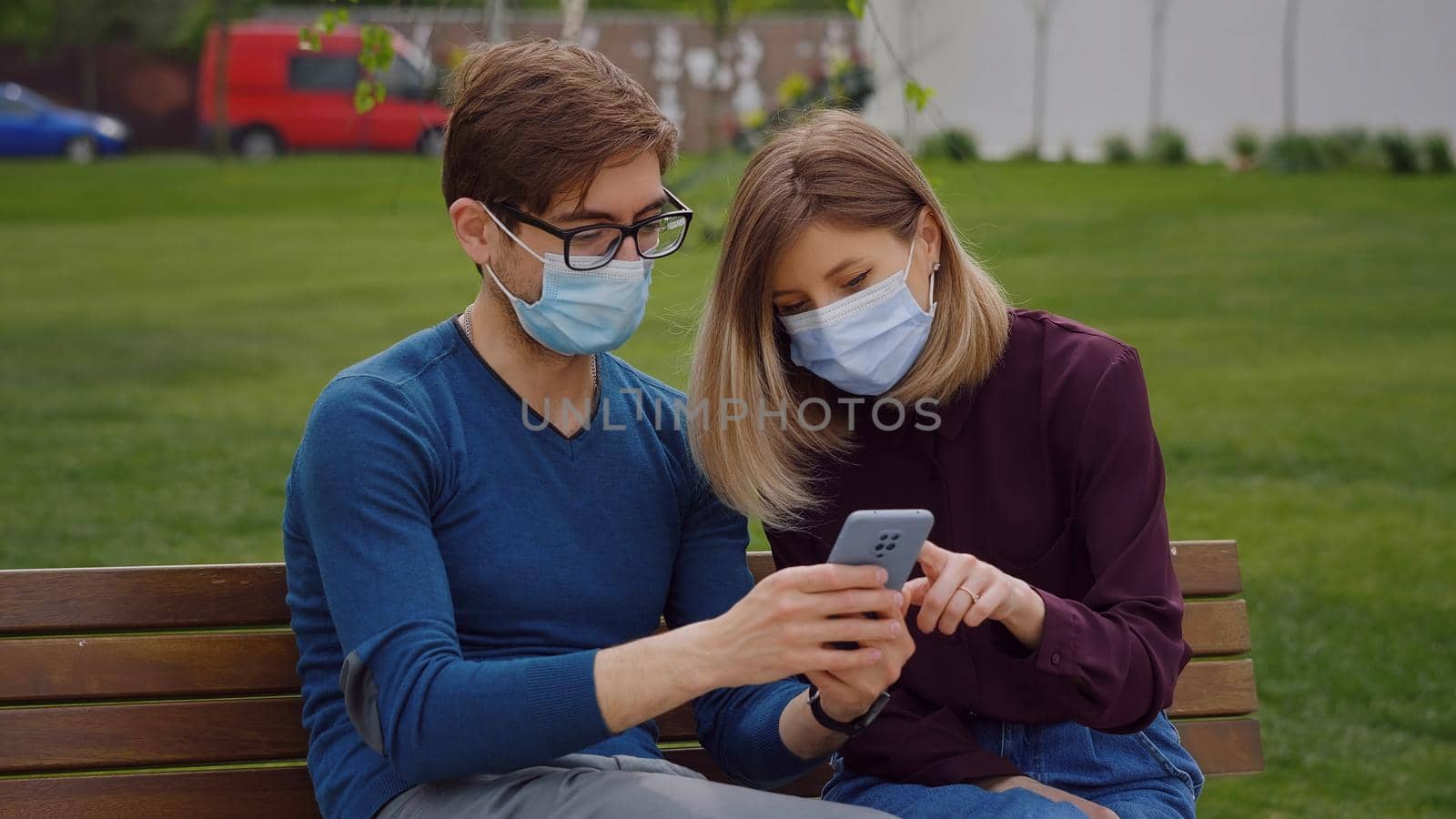 Two cute people look closely on phone and find out from news Couple sitting on bench, green background.