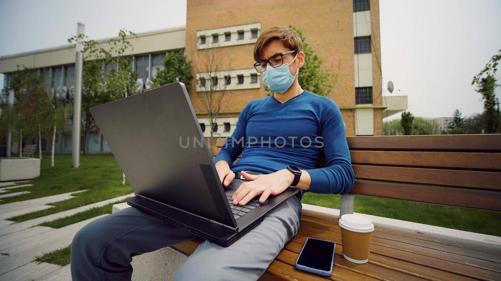 Young business man with mask using laptop. Handsome student studying on computer wearing protective mask resting at campus outdoors.