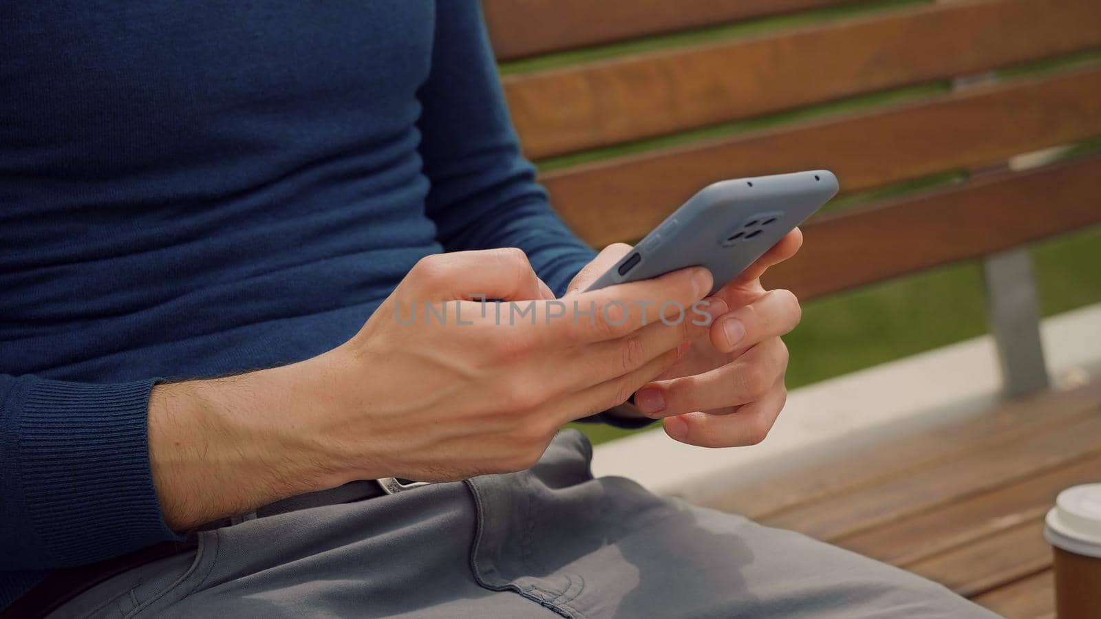 Man using mobile phone. Writing a message on smartphone outdoor park. Downloading an app for his mobile phone. Holding a phone. Use technology.