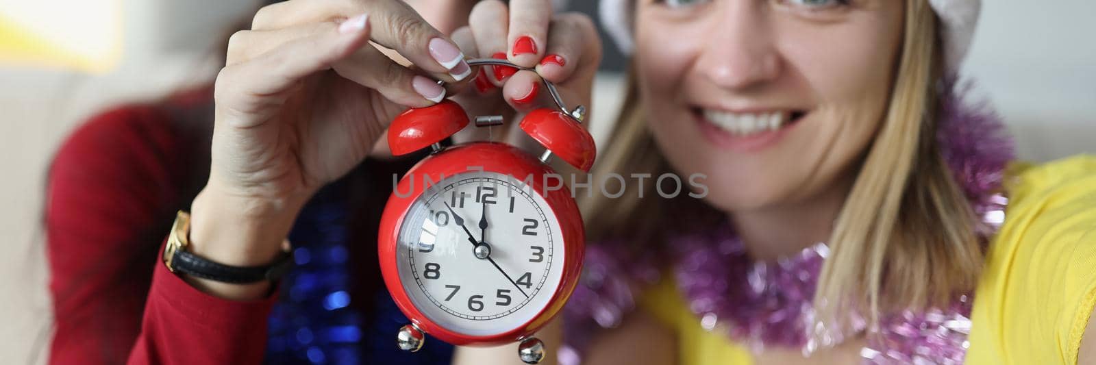 Sisters smile and hold red retro clock with arrows placed on midnight by kuprevich
