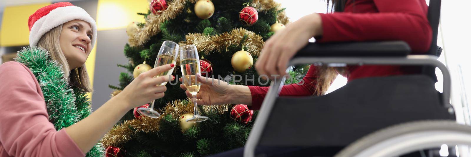 Low angle of sisters clink with glasses filled with champagne in cozy home atmosphere. Female meet new year and new life starts. Disabled people concept