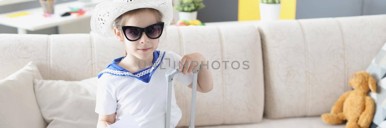 Portrait of little girl fashionista getting ready for summer vacation and perform scene. Child packed suitcase, wear sailor outfit. Summertime, fun concept