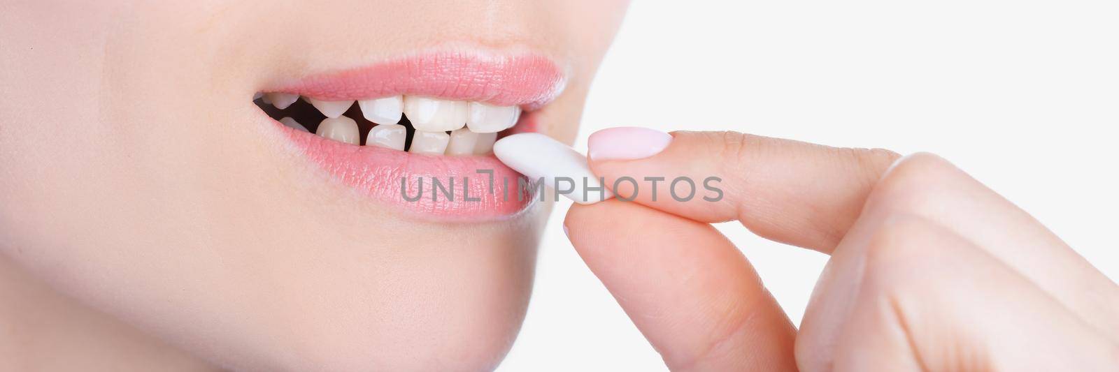 Close-up of womans face and female hand putting into mouth chewing gum. Lady enjoying sweet gum for fresh breath. Teethcare, health, dentistry concept