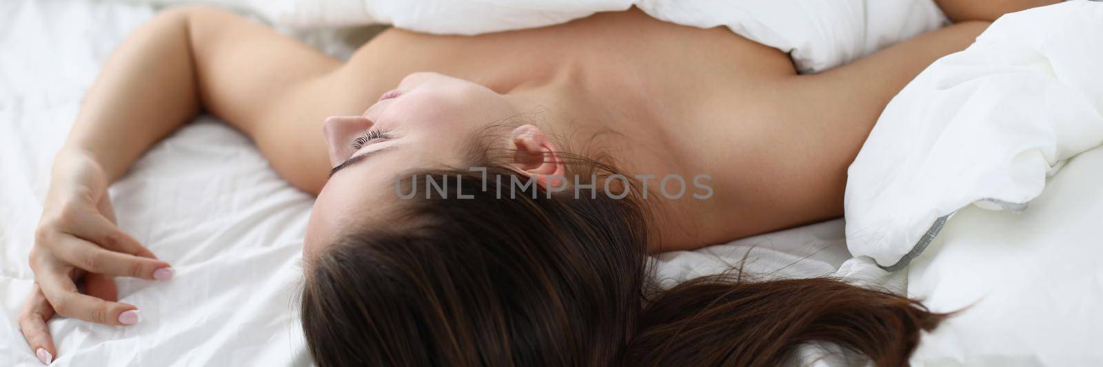 Close-up of relaxed brunette woman sleeping topless on white bedding at home. Tired after long working day, see nice dreams, napping. Good morning concept